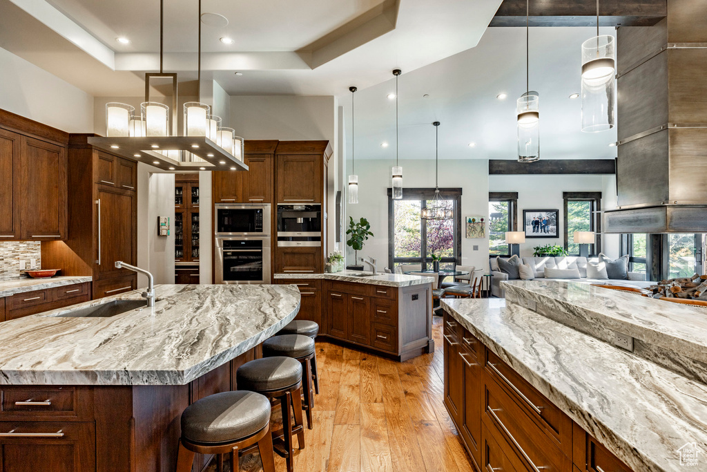 Kitchen featuring a sink, light wood-style floors, a spacious island, appliances with stainless steel finishes, and hanging light fixtures