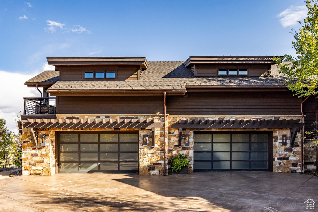 View of front facade with stone siding, concrete driveway, and a balcony