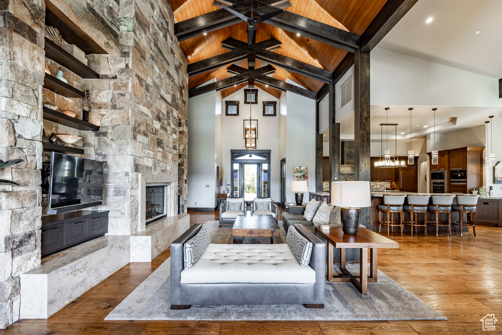Living room featuring high vaulted ceiling, a stone fireplace, wood finished floors, wooden ceiling with exposed beams, and a chandelier