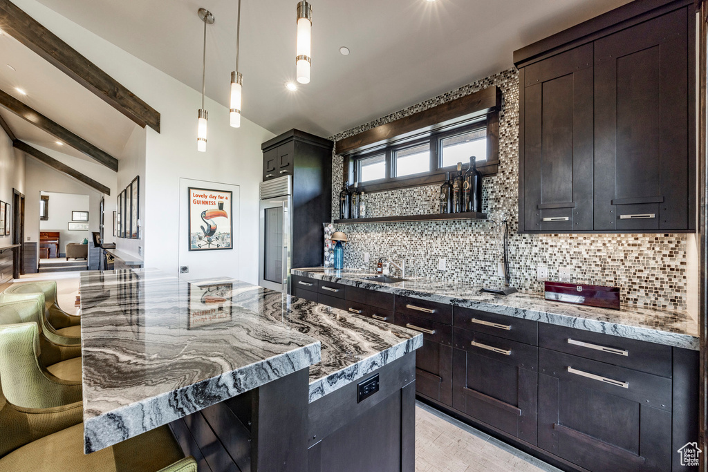 Kitchen featuring tasteful backsplash, light stone countertops, high end fridge, decorative light fixtures, and a sink