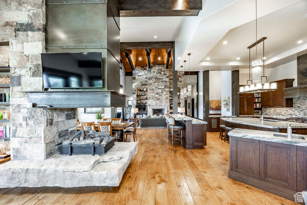 Living room with a stone fireplace, light wood-style flooring, and beamed ceiling