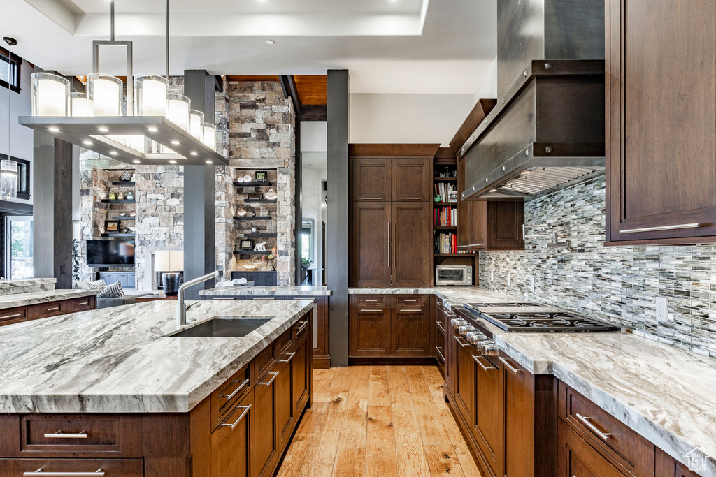 Kitchen with ventilation hood, a sink, light wood-style floors, tasteful backsplash, and an island with sink