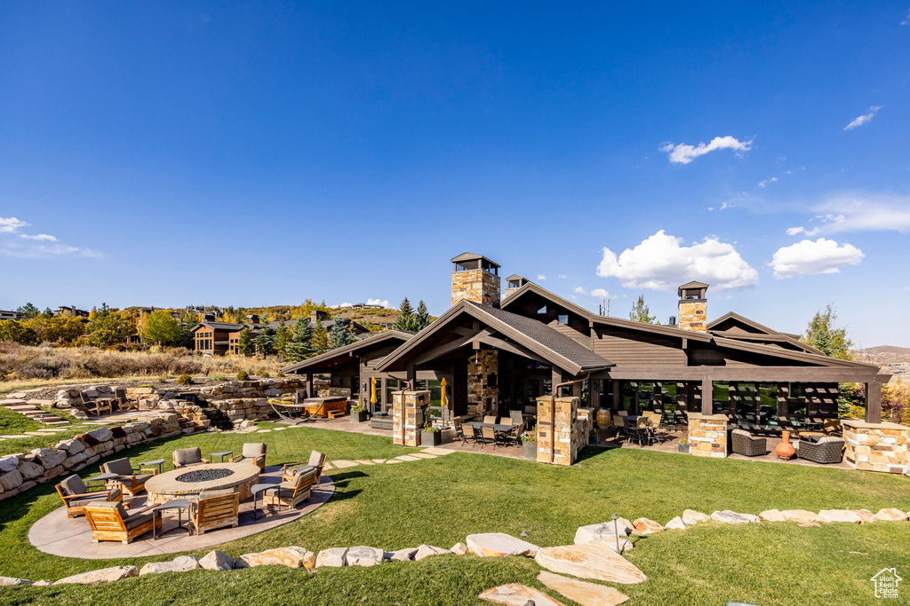 Back of house with a chimney, a patio, a lawn, stone siding, and an outdoor living space with a fire pit