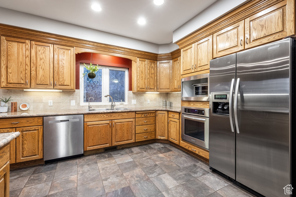 Kitchen featuring decorative backsplash, stainless steel appliances, sink, and light stone counters