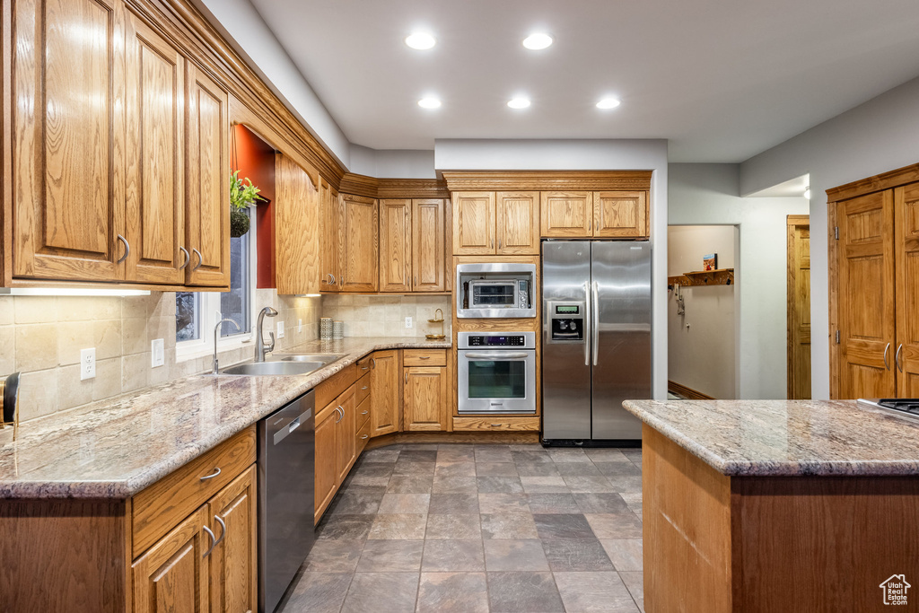 Kitchen featuring light stone counters, stainless steel appliances, sink, and backsplash