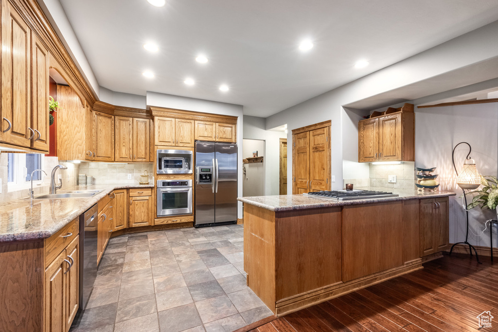 Kitchen featuring kitchen peninsula, decorative backsplash, appliances with stainless steel finishes, wood-type flooring, and sink