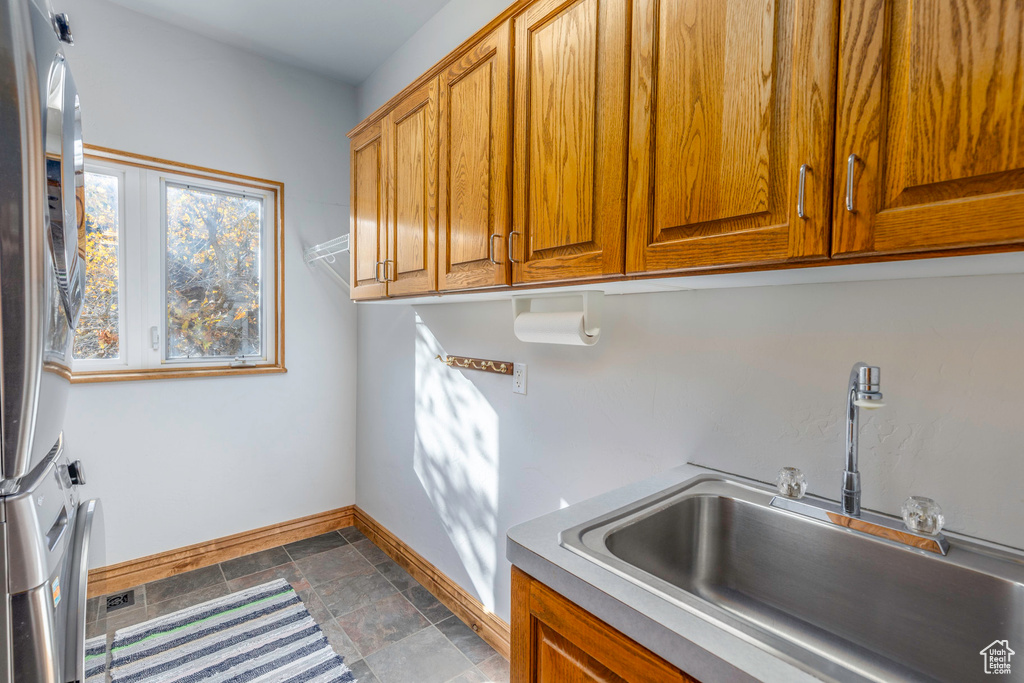 Clothes washing area with sink, stacked washer / dryer, and cabinets