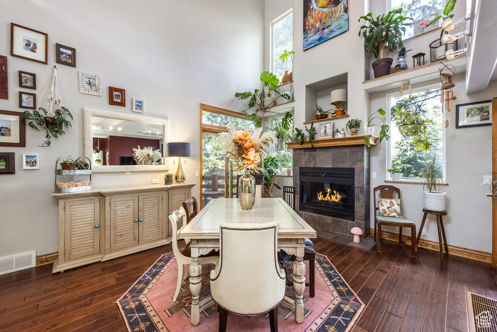 Dining space featuring a towering ceiling, a tile fireplace, and dark wood-style floors
