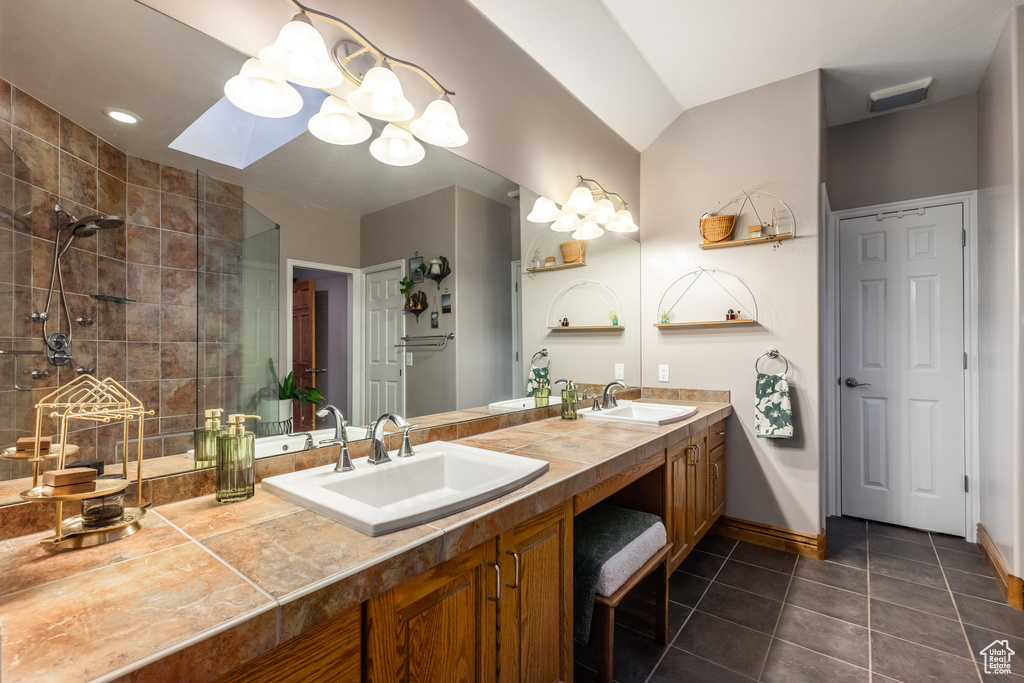 Bathroom featuring vanity, a tile shower, tile patterned flooring, and lofted ceiling with skylight