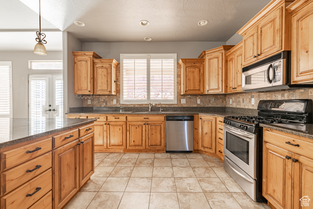 Kitchen with sink, backsplash, hanging light fixtures, stainless steel appliances, and light tile patterned floors