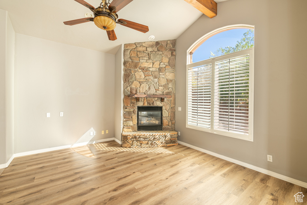 Unfurnished living room with a stone fireplace, light hardwood / wood-style flooring, lofted ceiling with beams, and ceiling fan