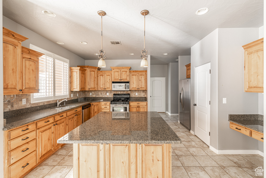 Kitchen with decorative backsplash, appliances with stainless steel finishes, dark stone counters, and a kitchen island