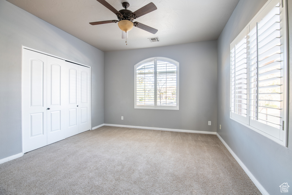 Unfurnished bedroom with a closet, ceiling fan, multiple windows, and carpet floors