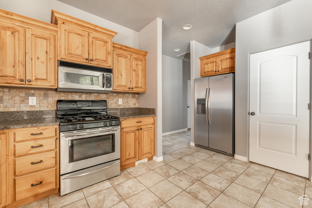 Kitchen featuring appliances with stainless steel finishes, dark stone countertops, tasteful backsplash, and light brown cabinetry