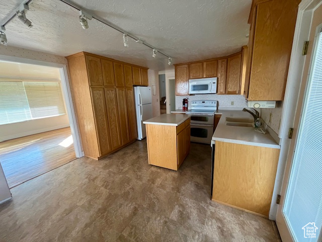 Kitchen with sink, a center island, rail lighting, a textured ceiling, and white appliances