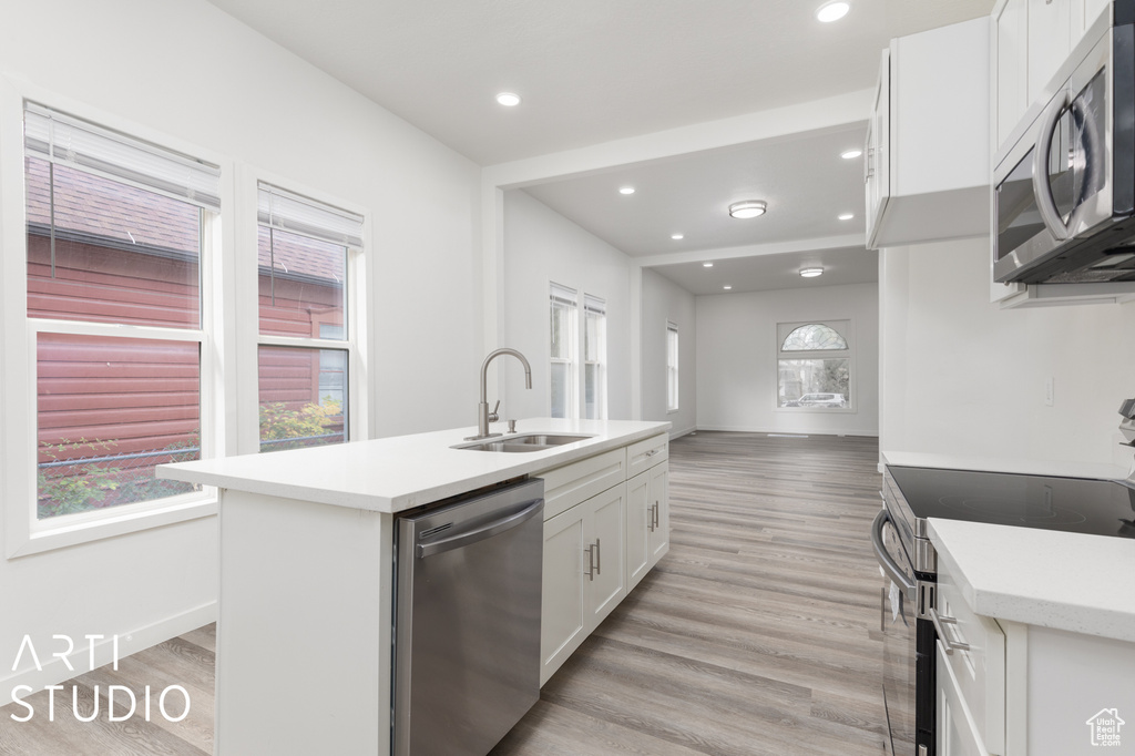 Kitchen with a center island with sink, sink, light wood-type flooring, white cabinetry, and appliances with stainless steel finishes