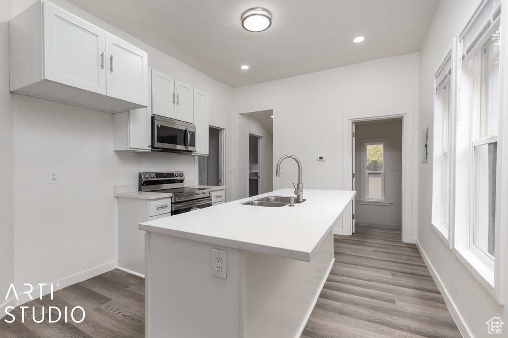 Kitchen featuring a kitchen island with sink, sink, white cabinetry, appliances with stainless steel finishes, and light hardwood / wood-style floors