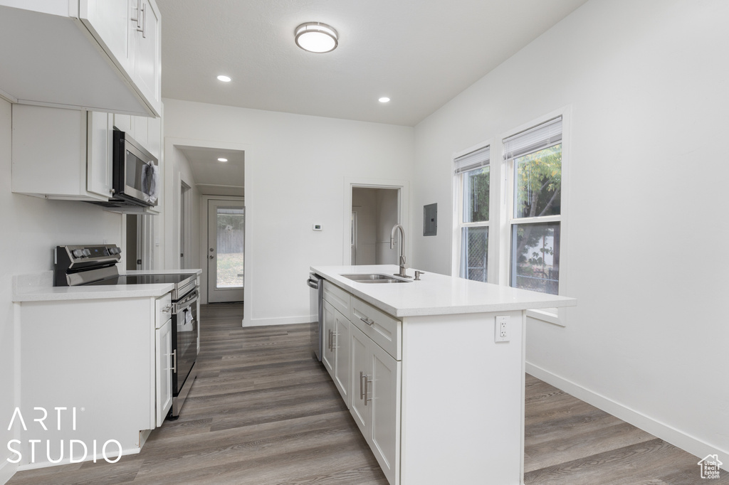 Kitchen featuring appliances with stainless steel finishes, hardwood / wood-style flooring, sink, and an island with sink