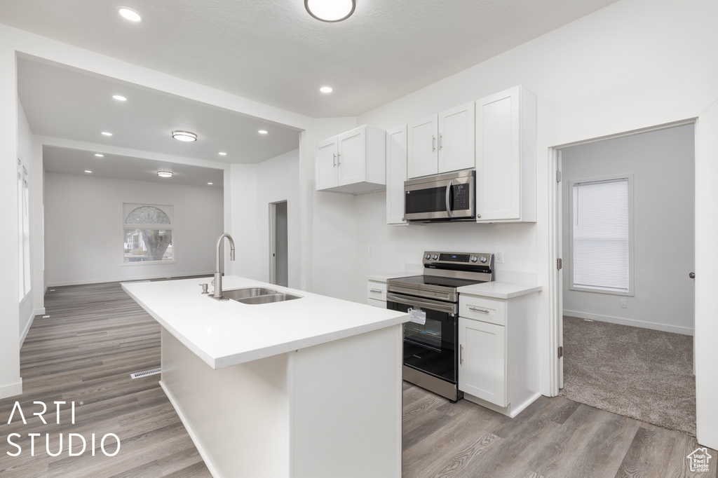 Kitchen with white cabinets, an island with sink, appliances with stainless steel finishes, light wood-type flooring, and sink