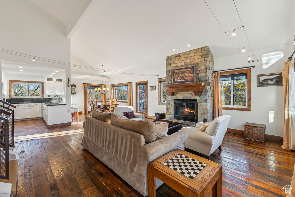 Living room featuring a notable chandelier, a stone fireplace, wood-type flooring, and high vaulted ceiling