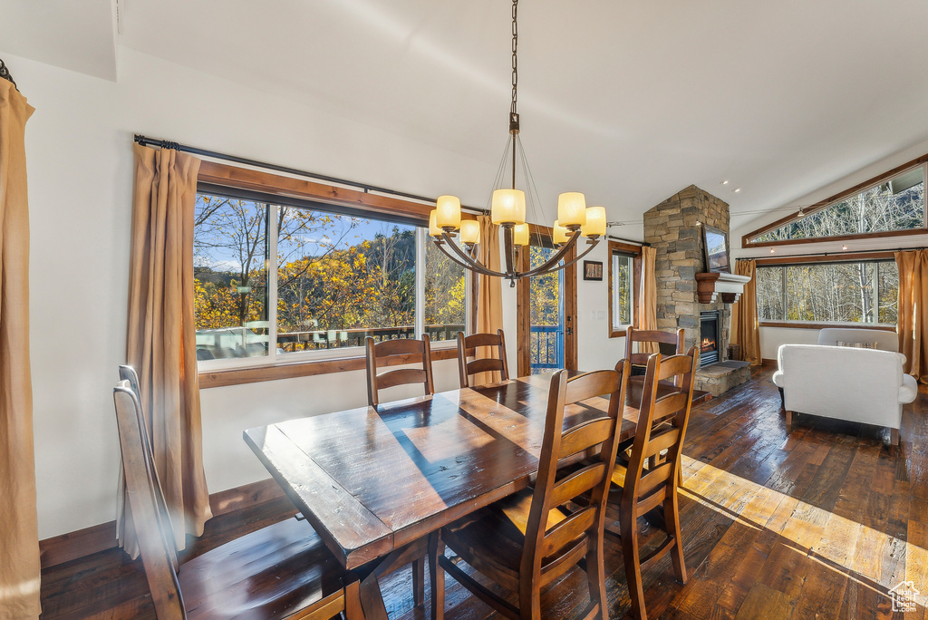 Dining room featuring a stone fireplace, vaulted ceiling, a wealth of natural light, and dark hardwood / wood-style floors