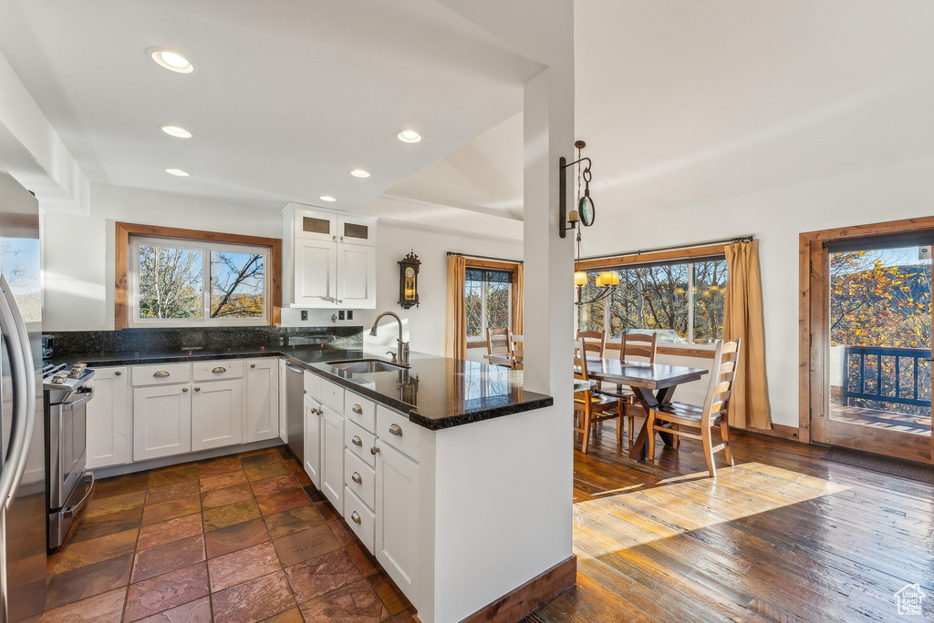 Kitchen with white cabinets, sink, dark stone counters, stainless steel stove, and dark wood-type flooring