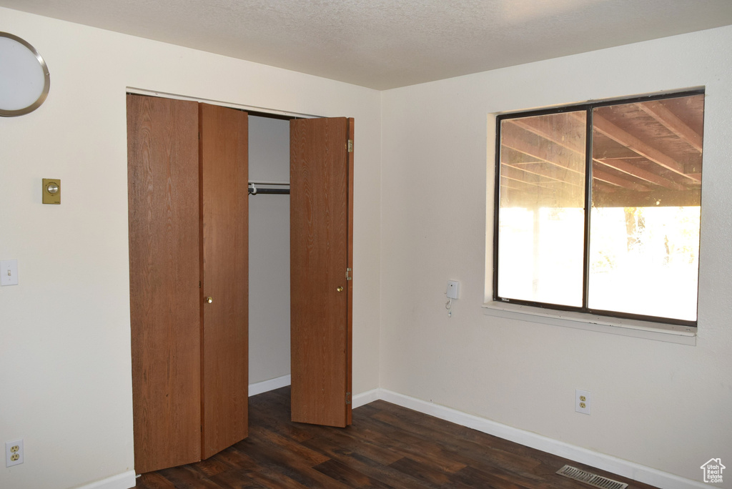 Unfurnished bedroom featuring a closet, a textured ceiling, and dark hardwood / wood-style flooring