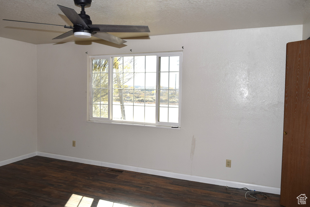 Empty room featuring a textured ceiling, dark wood-type flooring, and ceiling fan