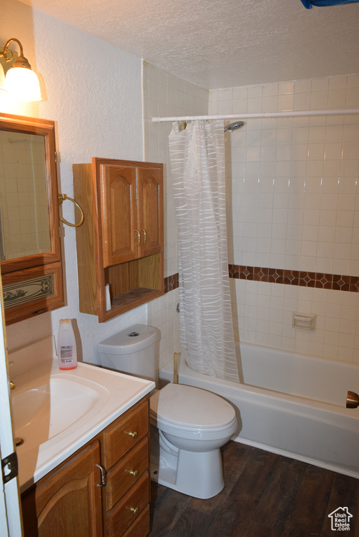 Full bathroom with a textured ceiling, shower / bath combination with curtain, toilet, vanity, and hardwood / wood-style flooring