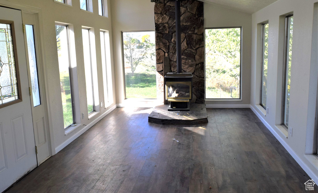 Unfurnished living room with dark hardwood / wood-style flooring, a wood stove, and a wealth of natural light