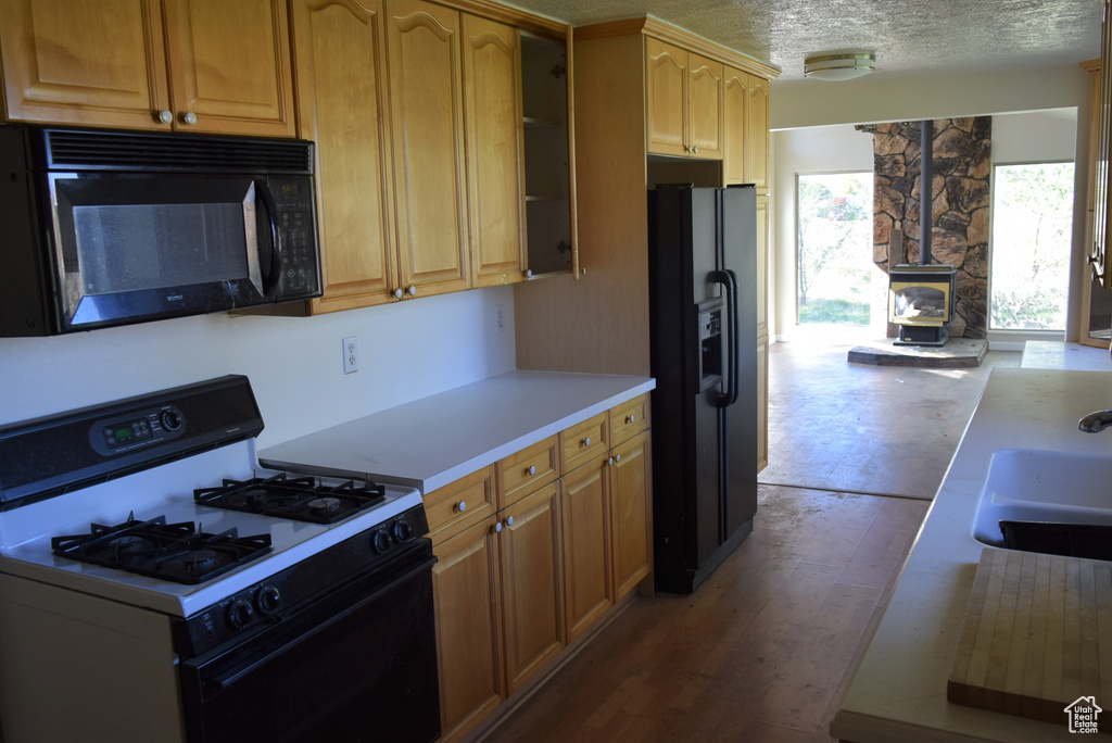 Kitchen with a wood stove, hardwood / wood-style floors, sink, black appliances, and a textured ceiling