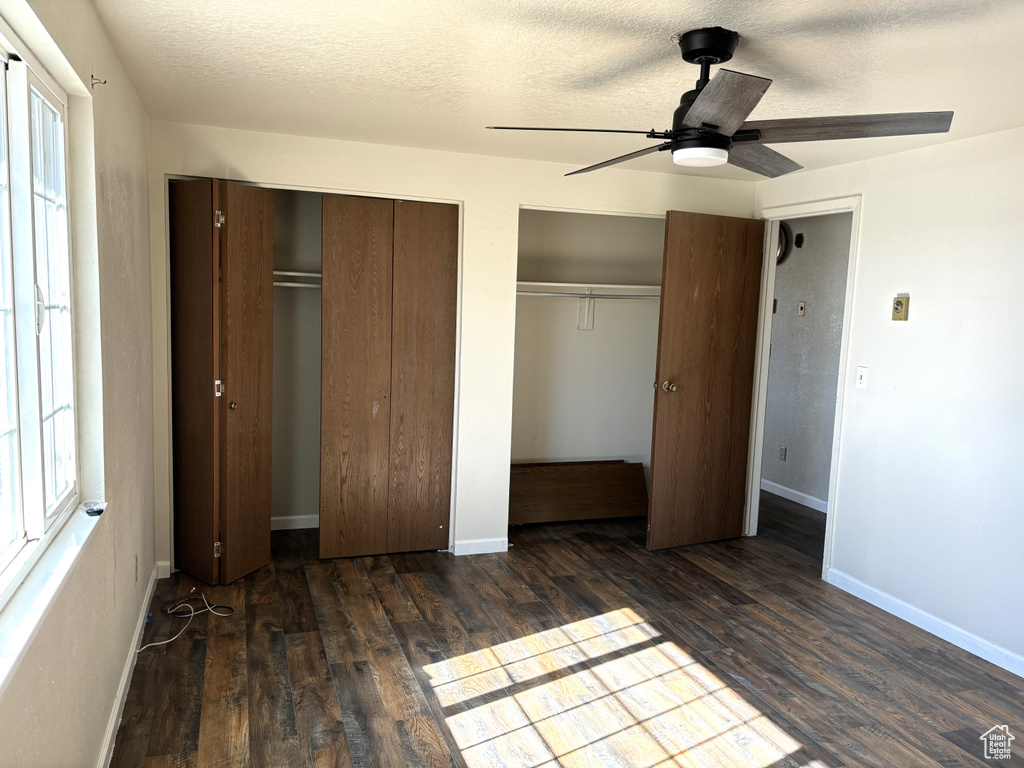 Unfurnished bedroom featuring dark wood-type flooring, two closets, a textured ceiling, and ceiling fan