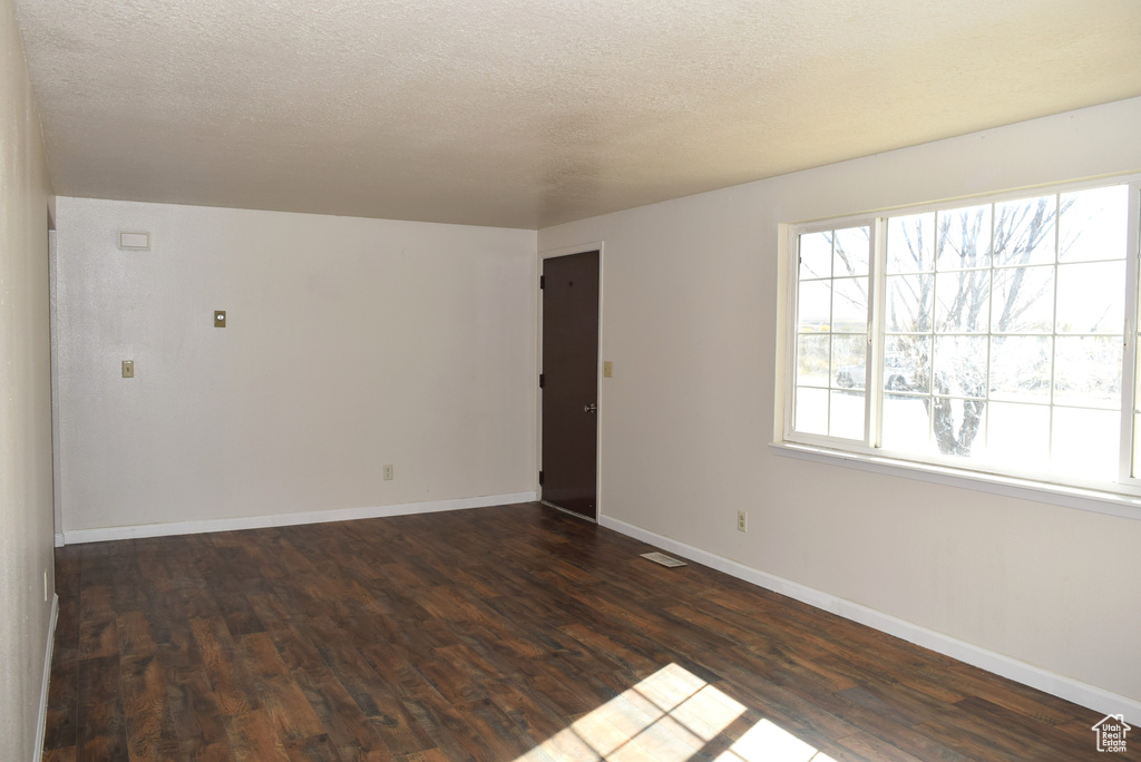 Empty room with dark hardwood / wood-style floors and a textured ceiling