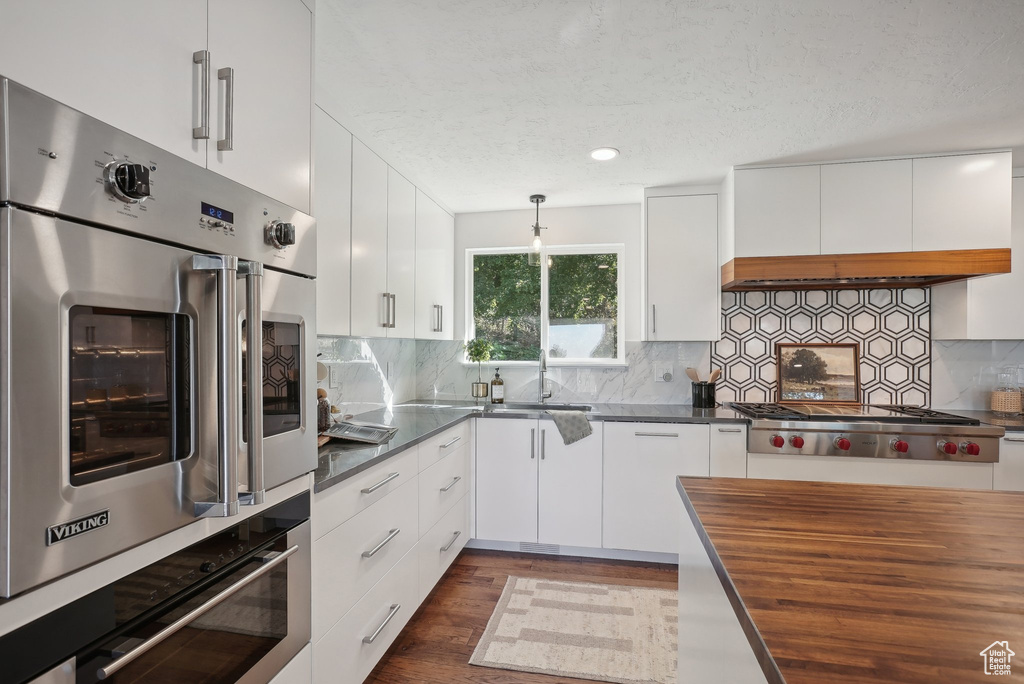 Kitchen featuring butcher block counters, decorative backsplash, and white cabinets