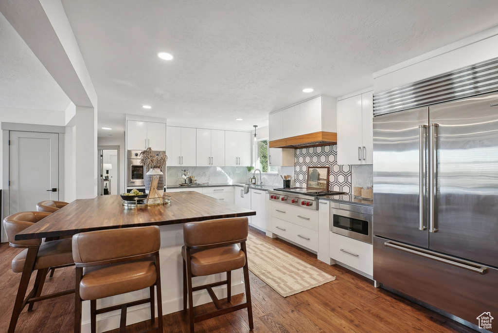 Kitchen with decorative backsplash, white cabinets, dark hardwood / wood-style flooring, stainless steel appliances, and a center island