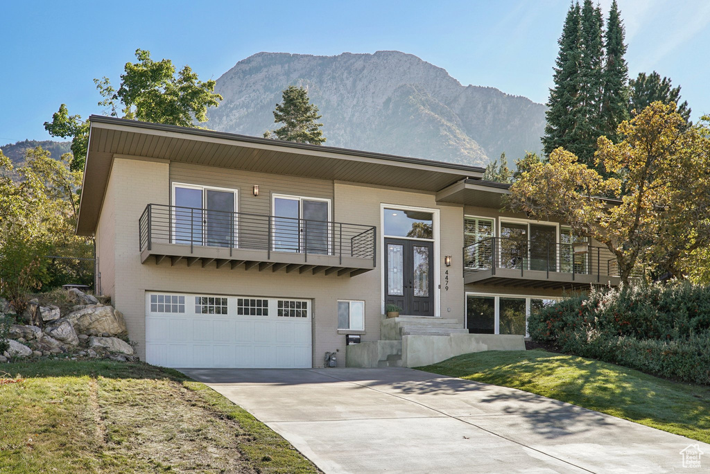 View of front of house with a mountain view, a front yard, a garage, and a balcony