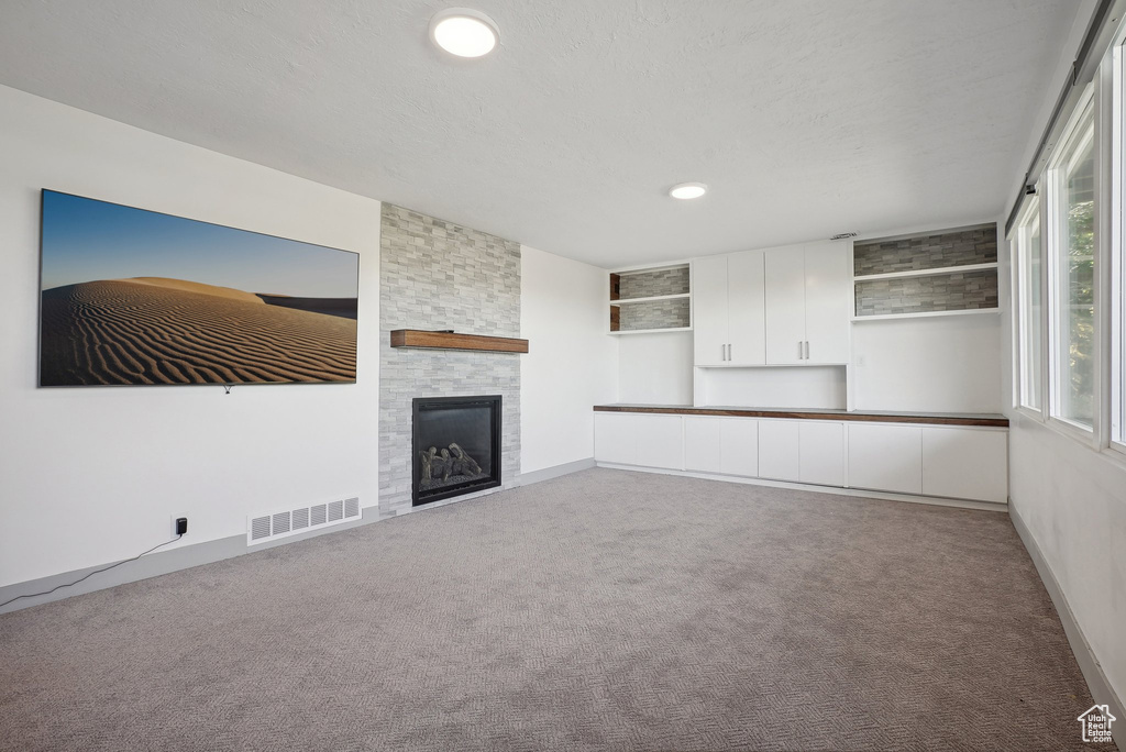 Unfurnished living room featuring a stone fireplace and carpet flooring