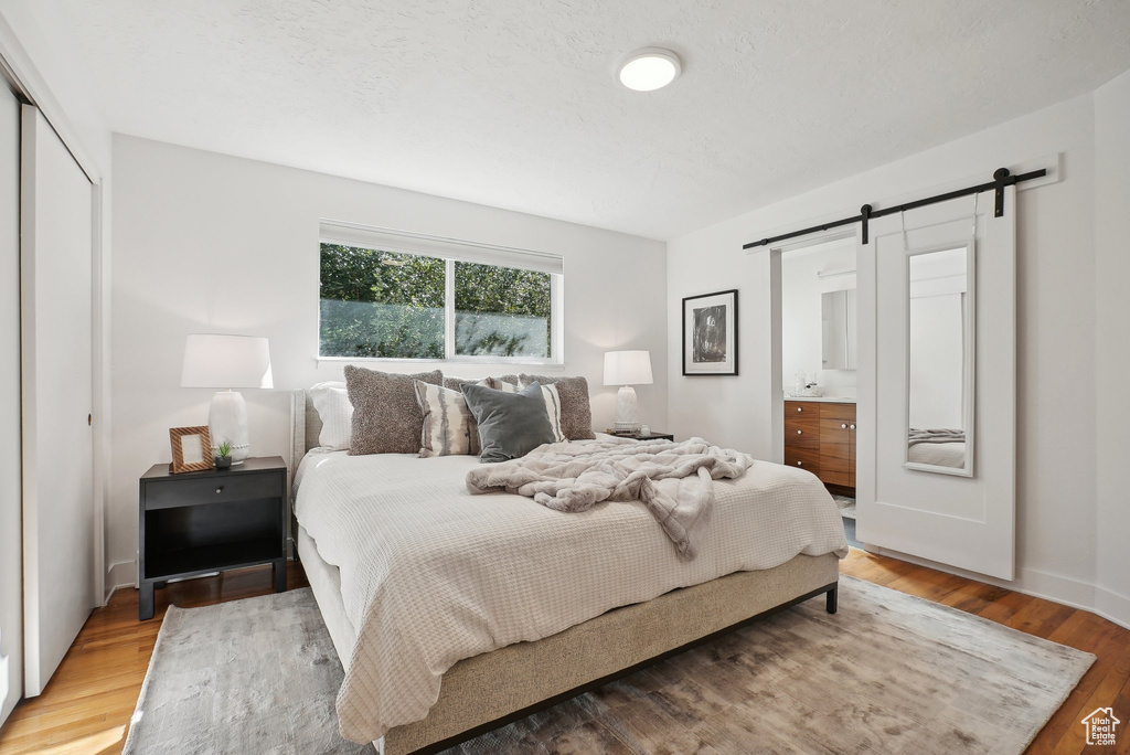 Bedroom featuring a closet, ensuite bathroom, a barn door, and hardwood / wood-style floors