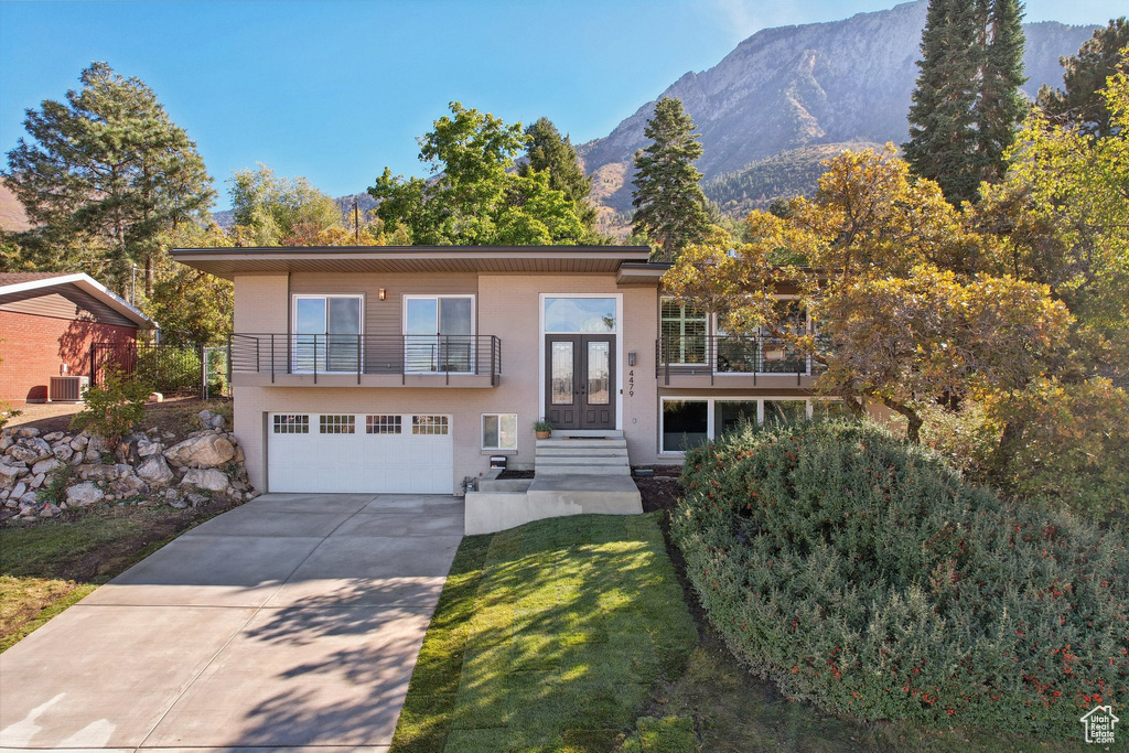 View of front facade featuring a garage, central air condition unit, a mountain view, a balcony, and a front yard