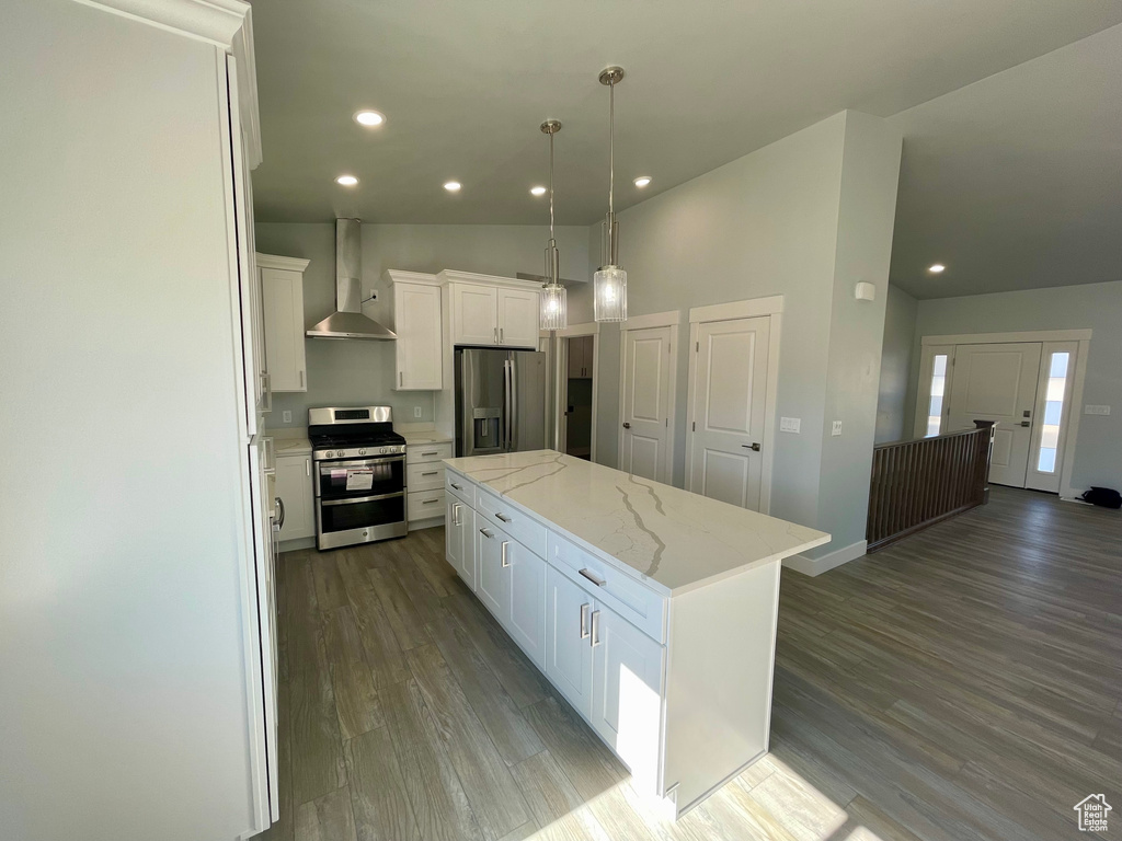 Kitchen featuring appliances with stainless steel finishes, a center island, wall chimney exhaust hood, white cabinets, and hardwood / wood-style flooring