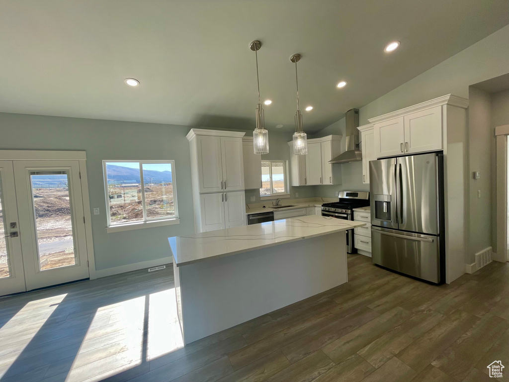 Kitchen with wall chimney exhaust hood, white cabinets, stainless steel appliances, and a wealth of natural light