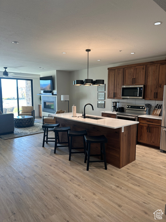 Kitchen featuring appliances with stainless steel finishes, sink, light wood-type flooring, decorative light fixtures, and a center island with sink