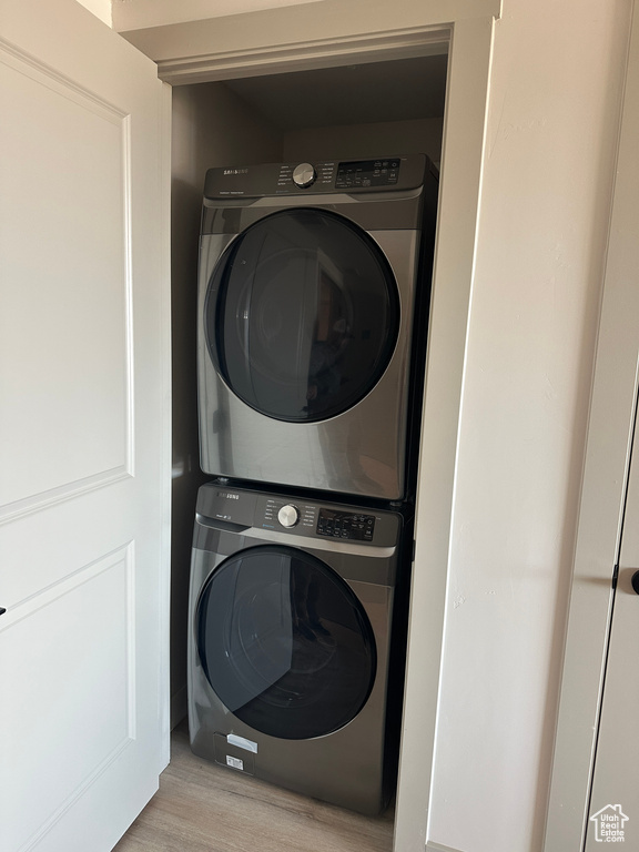 Laundry room with light hardwood / wood-style flooring and stacked washer and clothes dryer