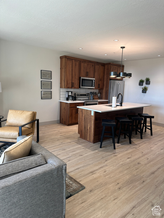 Kitchen featuring a breakfast bar area, light hardwood / wood-style flooring, an island with sink, pendant lighting, and appliances with stainless steel finishes