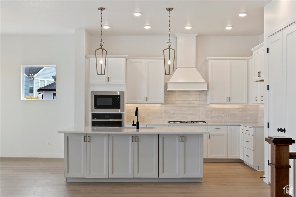 Kitchen featuring appliances with stainless steel finishes, hanging light fixtures, white cabinetry, and an island with sink