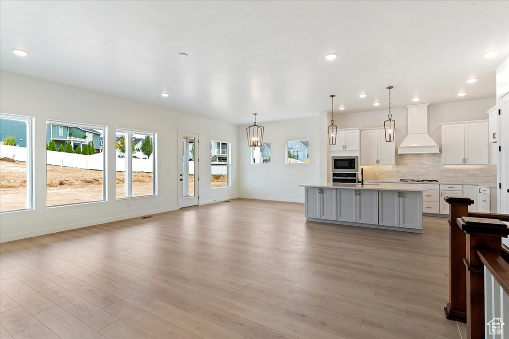 Kitchen featuring light hardwood / wood-style floors, pendant lighting, white cabinets, custom range hood, and a kitchen island with sink