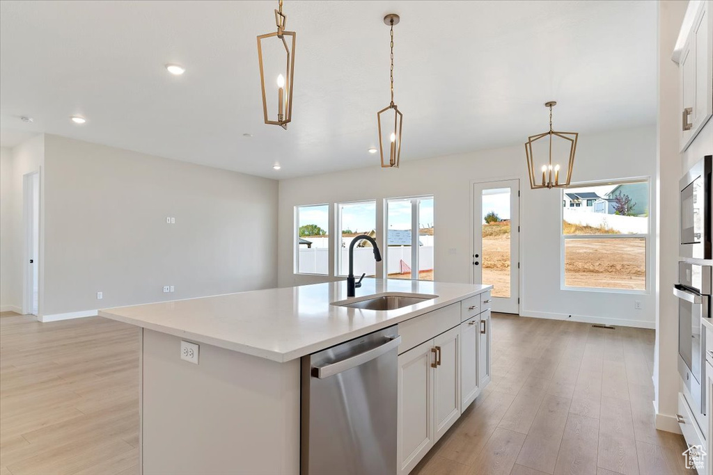 Kitchen with hanging light fixtures, a center island with sink, light wood-type flooring, sink, and stainless steel appliances