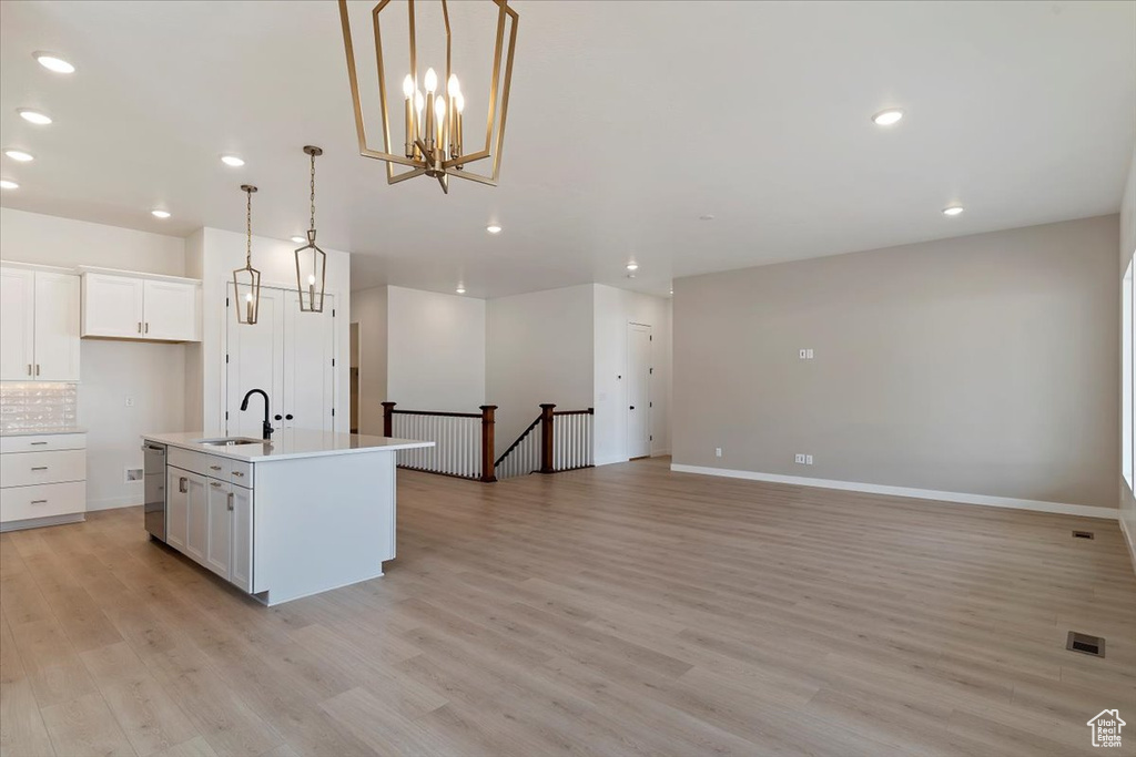 Kitchen featuring light hardwood / wood-style flooring, white cabinetry, pendant lighting, and an island with sink