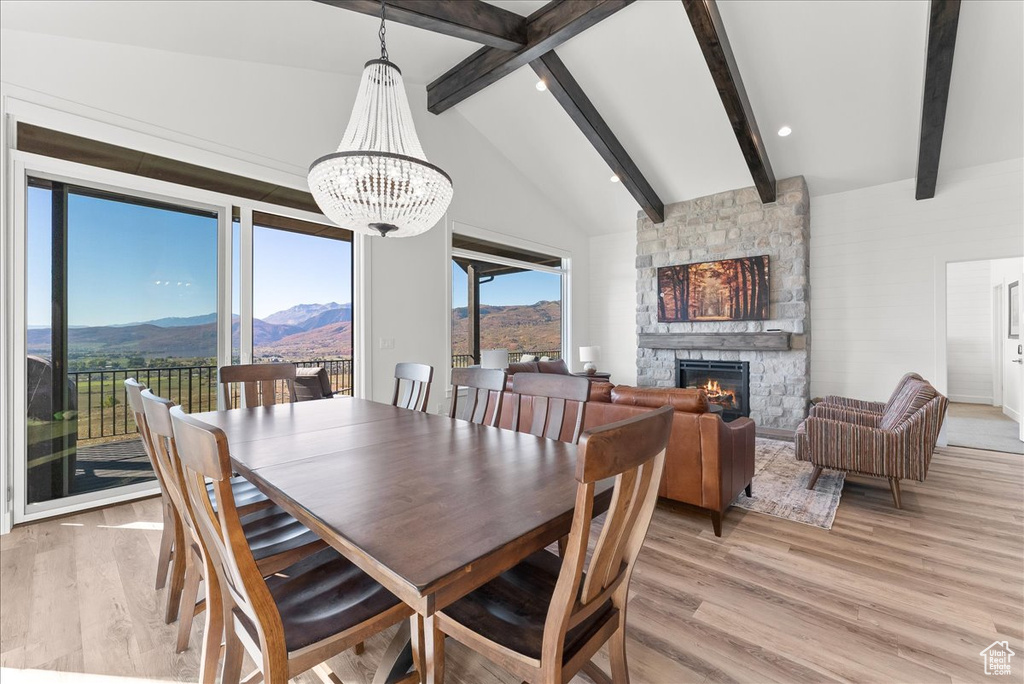 Dining space featuring light wood-type flooring, a fireplace, lofted ceiling with beams, a mountain view, and a chandelier