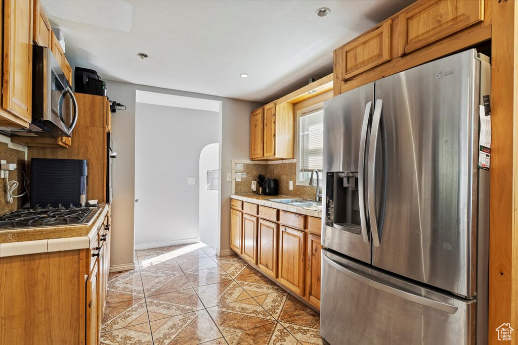 Kitchen with appliances with stainless steel finishes, tile countertops, tasteful backsplash, and sink